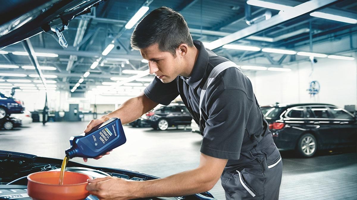 BMW service tech adding oil to engine.