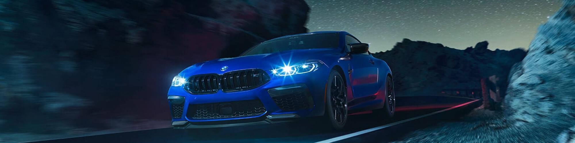 A blue BMW M8 driving along a highway at night.