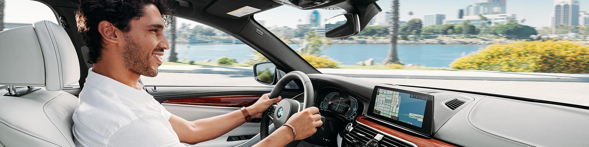 A smiling man driving his BMW 5 Series on a sunny day.