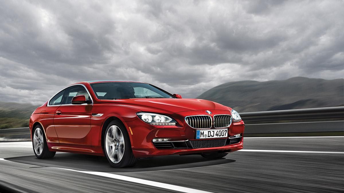 A red BMW Certified Pre-Owned 6 Series Coupe driving under stormy skies.