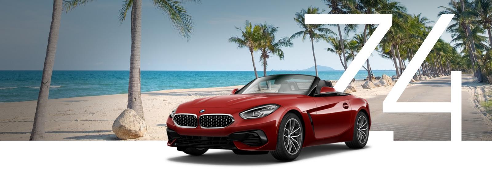 A red BMW Z4 parked on a road next to a tropical beach.