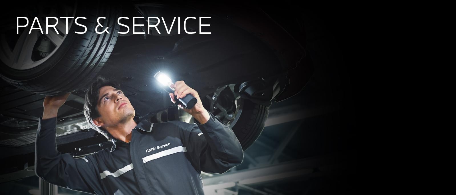 A certified BMW service technician inspecting under a car.
