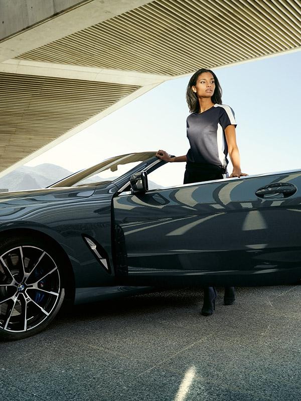 A woman standing in the open doorway of her BMW 8 Series Convertible.
