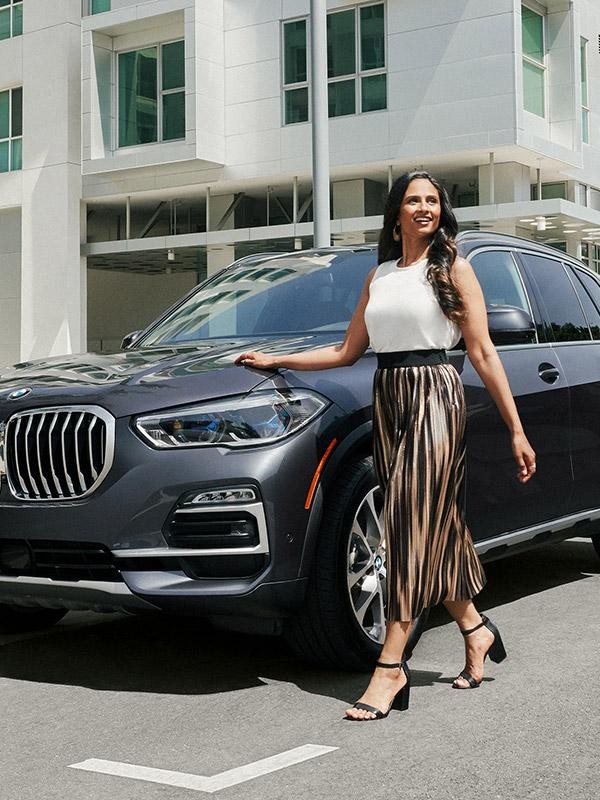 A smiling woman walking next to her new BMW X5 on a sunny day.