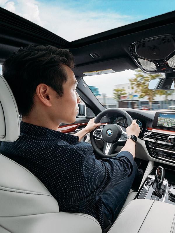 View of a man driving a BMW 3X from the rear seat point of view.