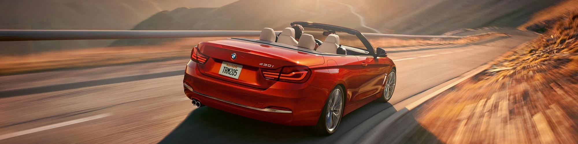 A red BMW 4 Series Convertible driving through the desert hills.
