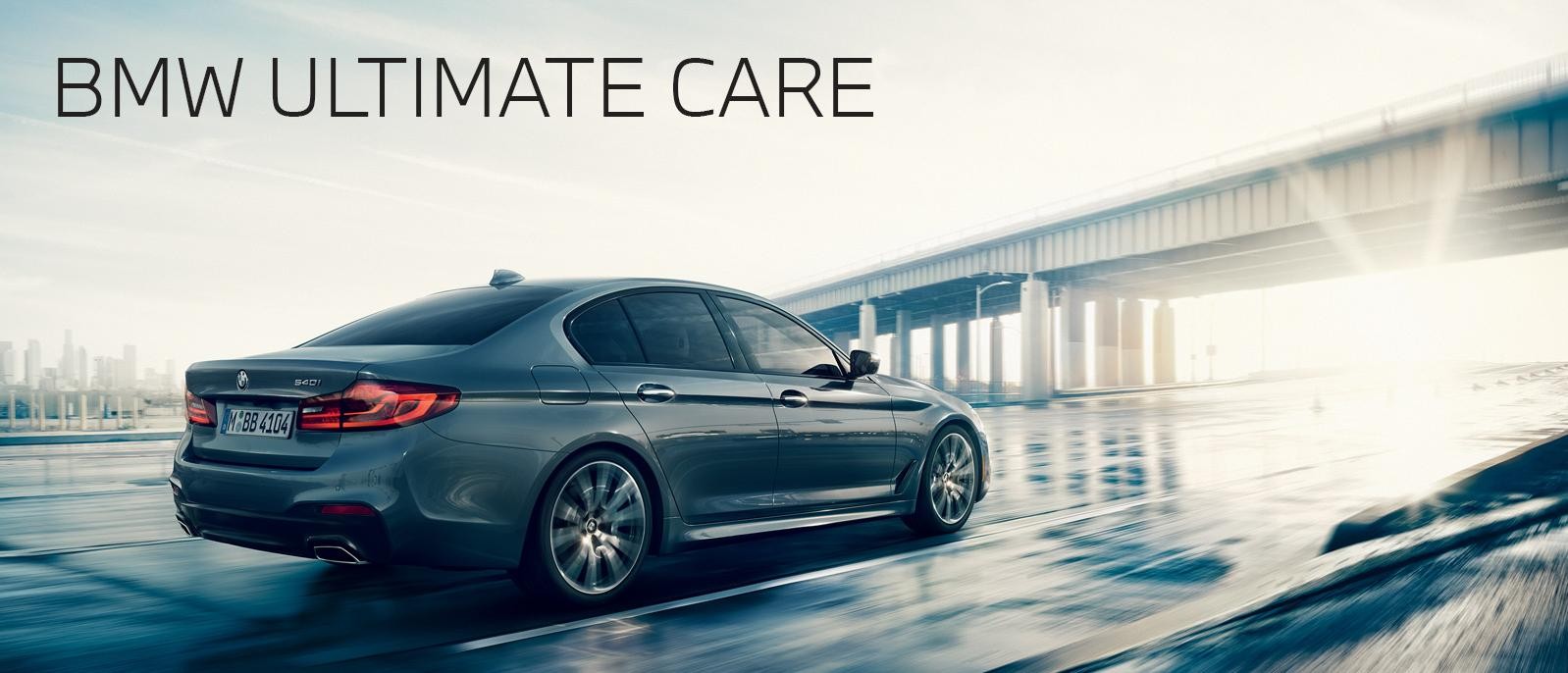A Grey BMW 5-Series sedan driving away from a city and into the sunset.