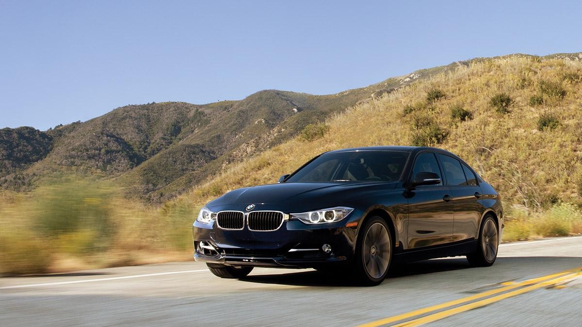 A black BMW certified pre-owned 3 Series driving down a desert highway.
