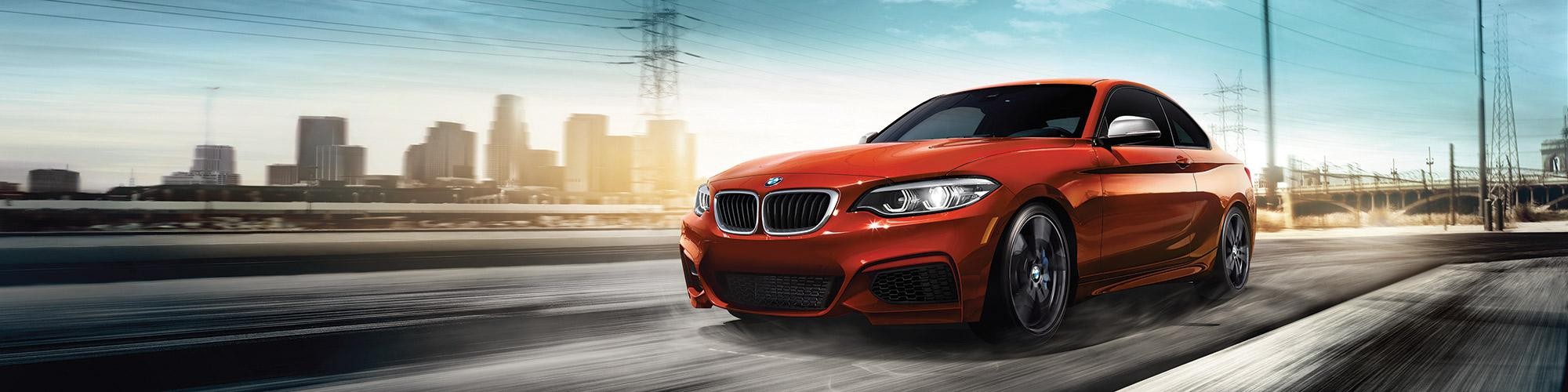 A red BMW 2 Series driving on a highway heading away from a city.