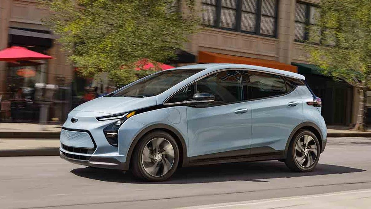 A light blue Chevy Bolt EV driving down a city street.