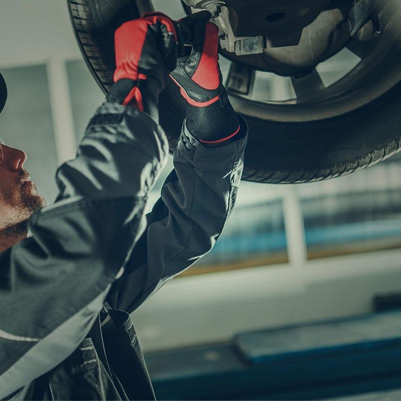 Car mechanic working on a wheel underneath a car.