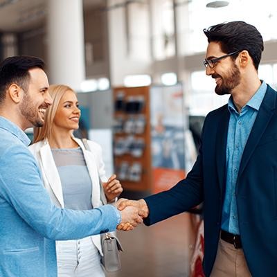 Couple at a dealership shaking hands with a sales associate