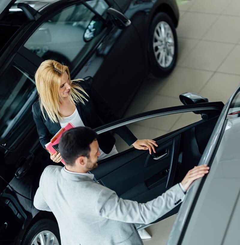 Dealership sales associate showing a customer a new car