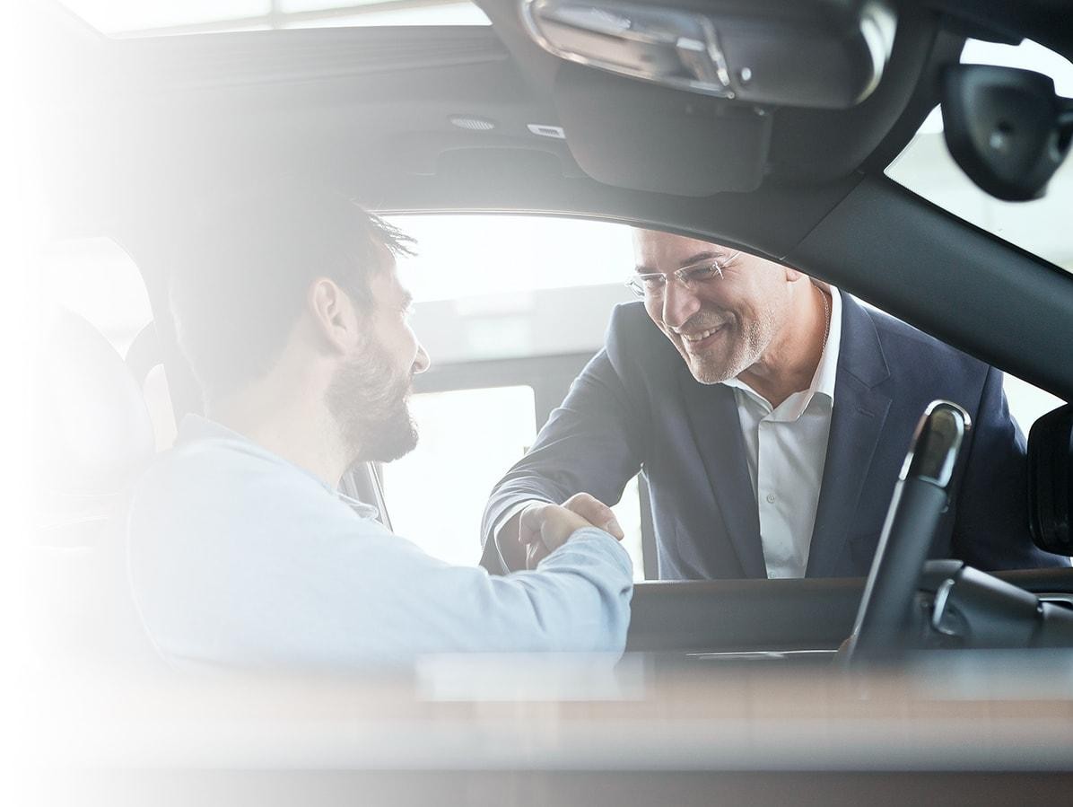 Dealership associate shaking hands with a customer in his new car