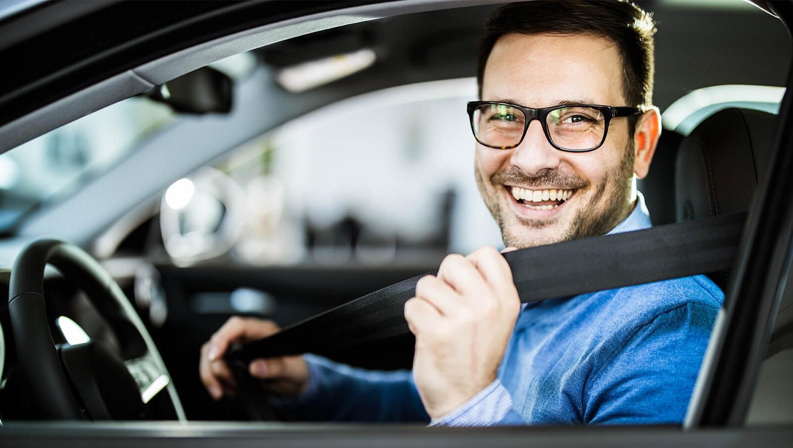 Smiling man in a car buckling his seat belt