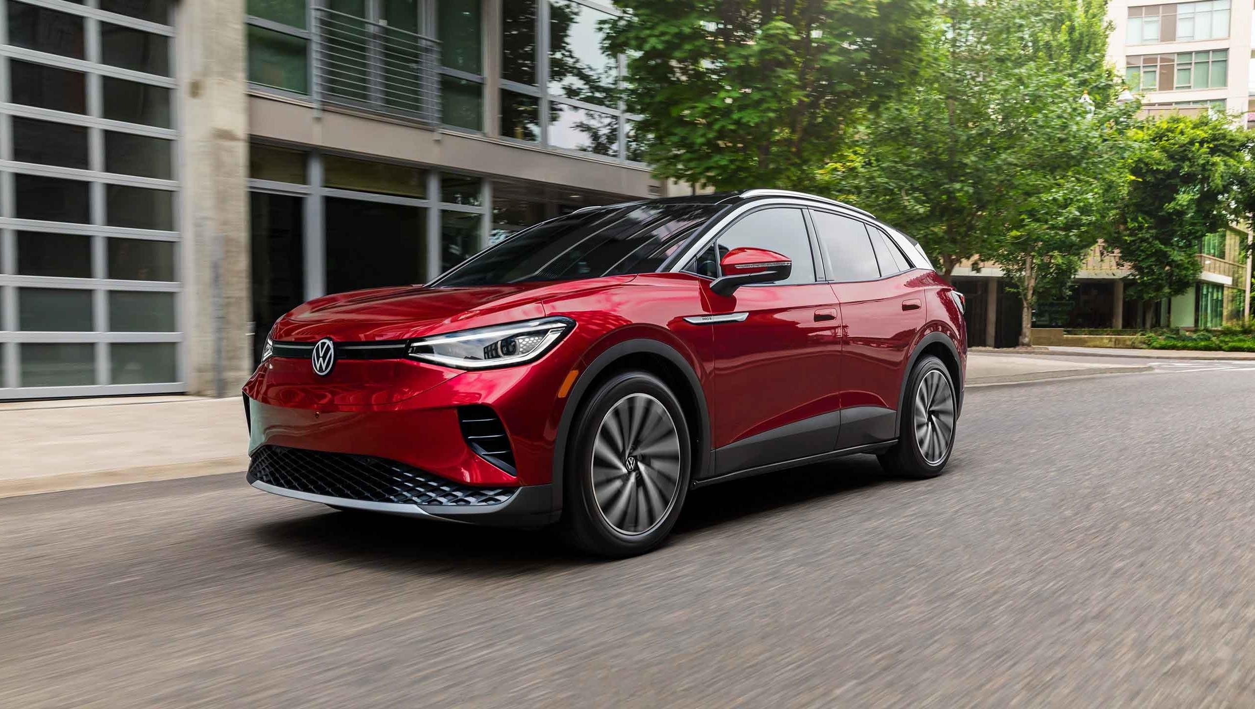 A ¾ front shot at street-level of an ID.4 SUV shown in Aurora Red Metallic, driving on a treelined, modern city street.