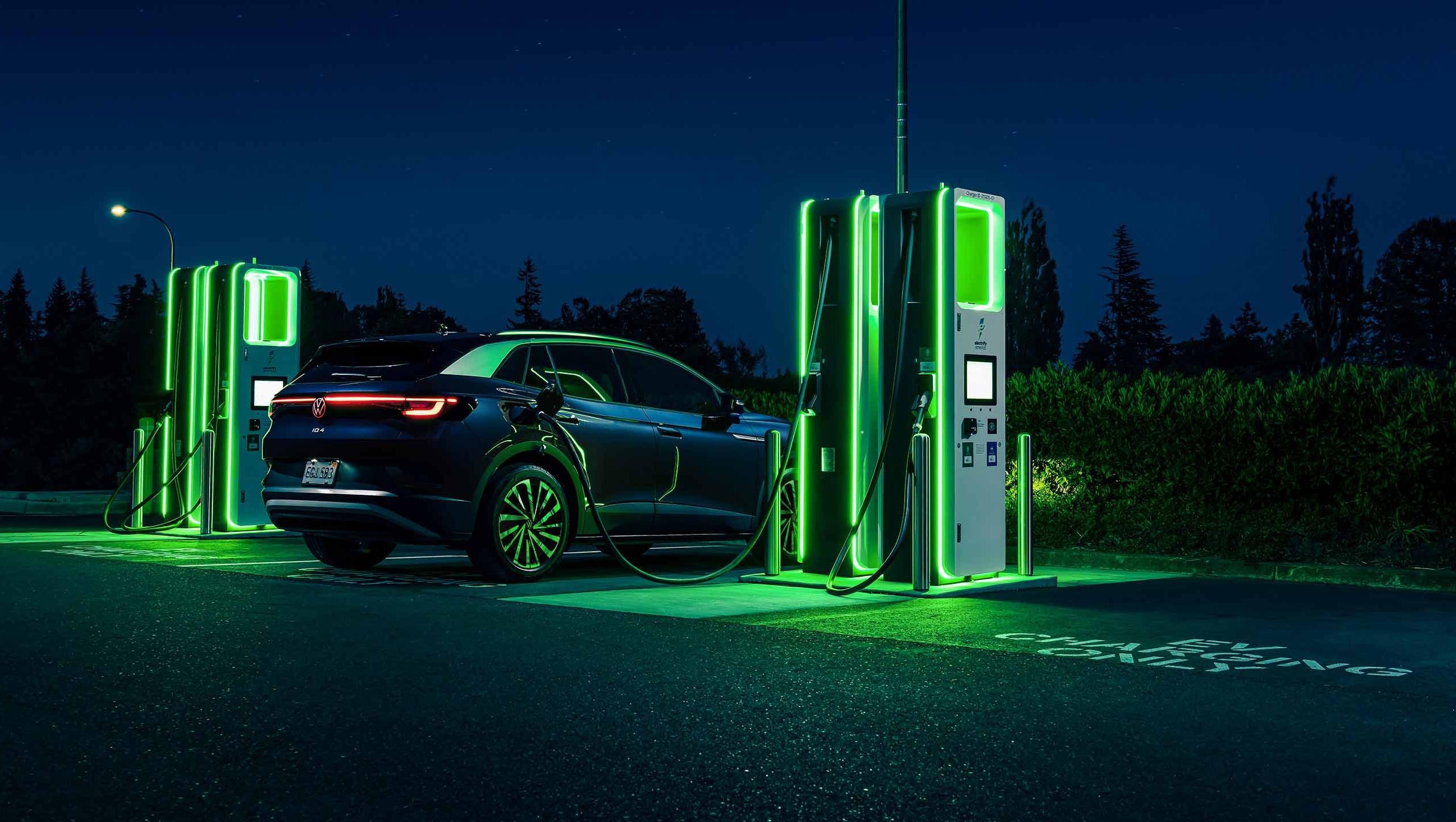 An ID.4 SUV in Tourmaline Blue Metallic is parked at night, charging at a neon lit charging station.