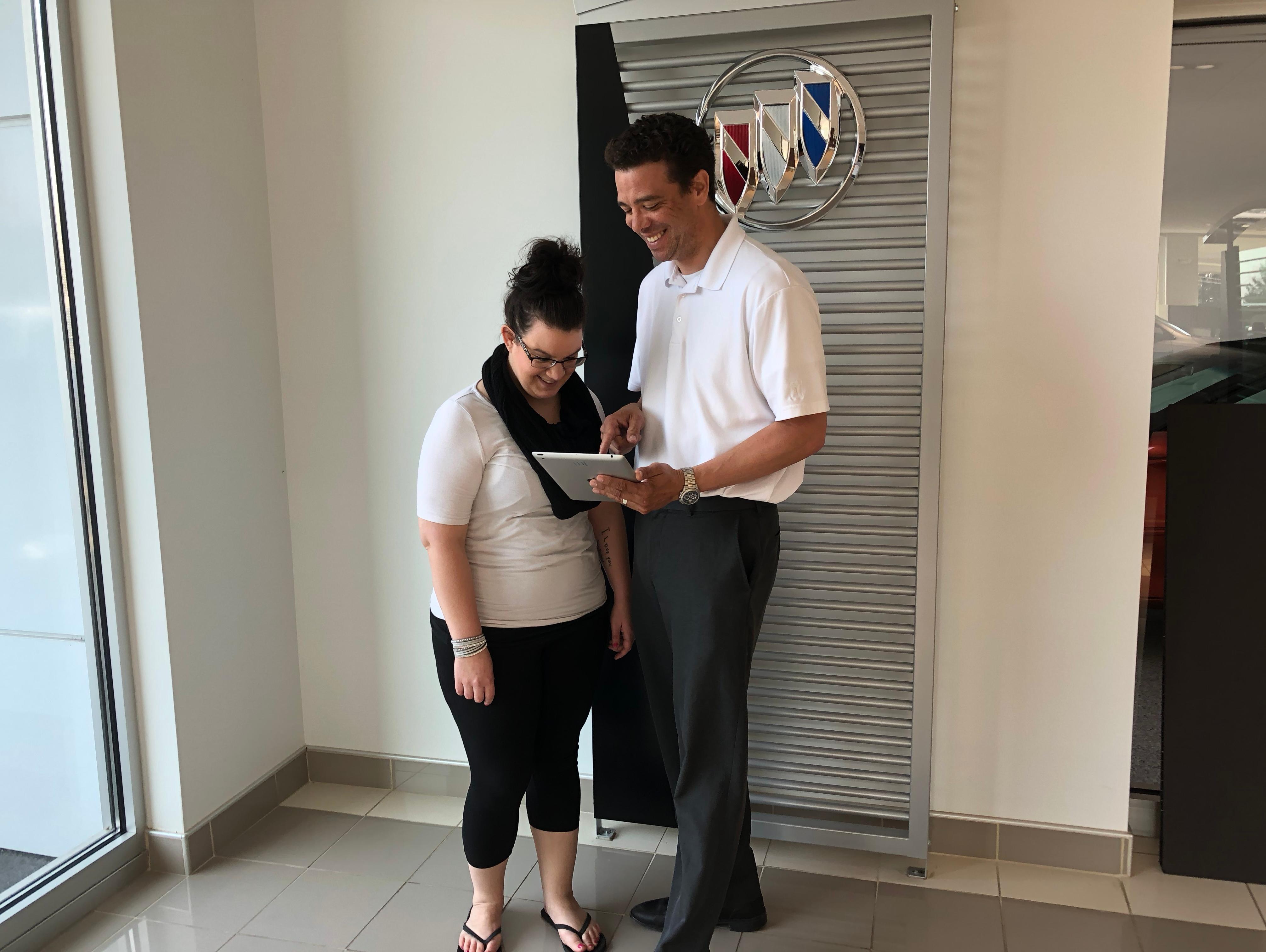 Two women looking at a tablet next to a new car.