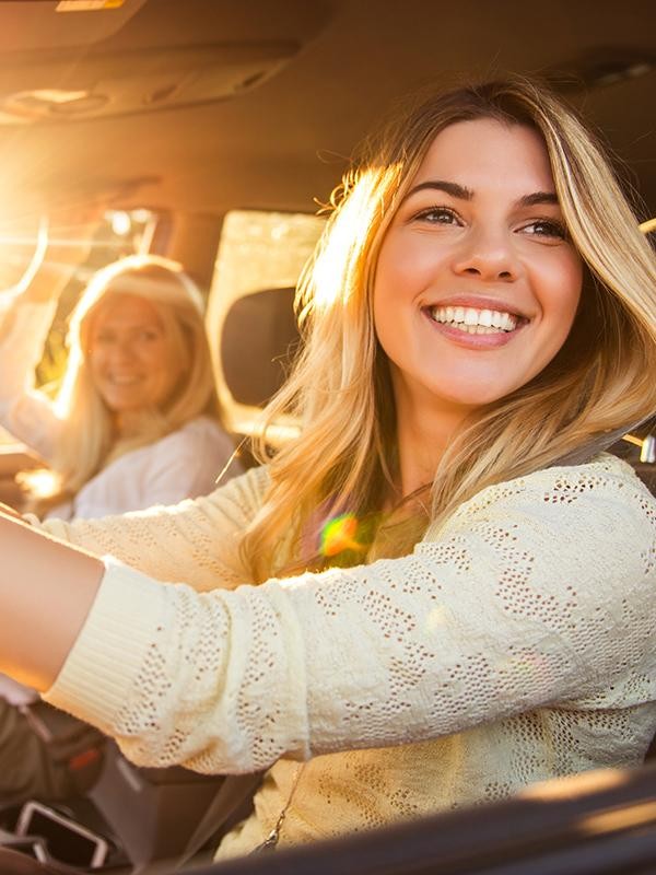 A young woman and her mother driving on a sunny afternoon.