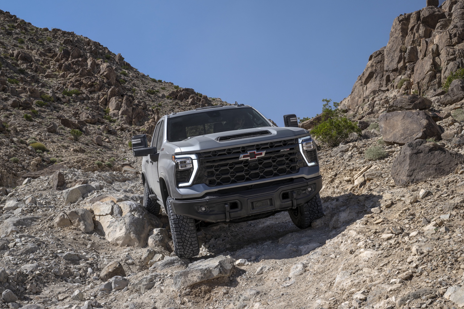 Gray 2024 Chevrolet Silverado HD pickup truck driving through rugged rocky terrain