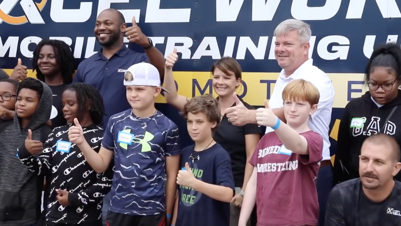 General Manager, Neal Wilson smiling, holding a thumbs up with members of the Xcel mobile training unit and school students.