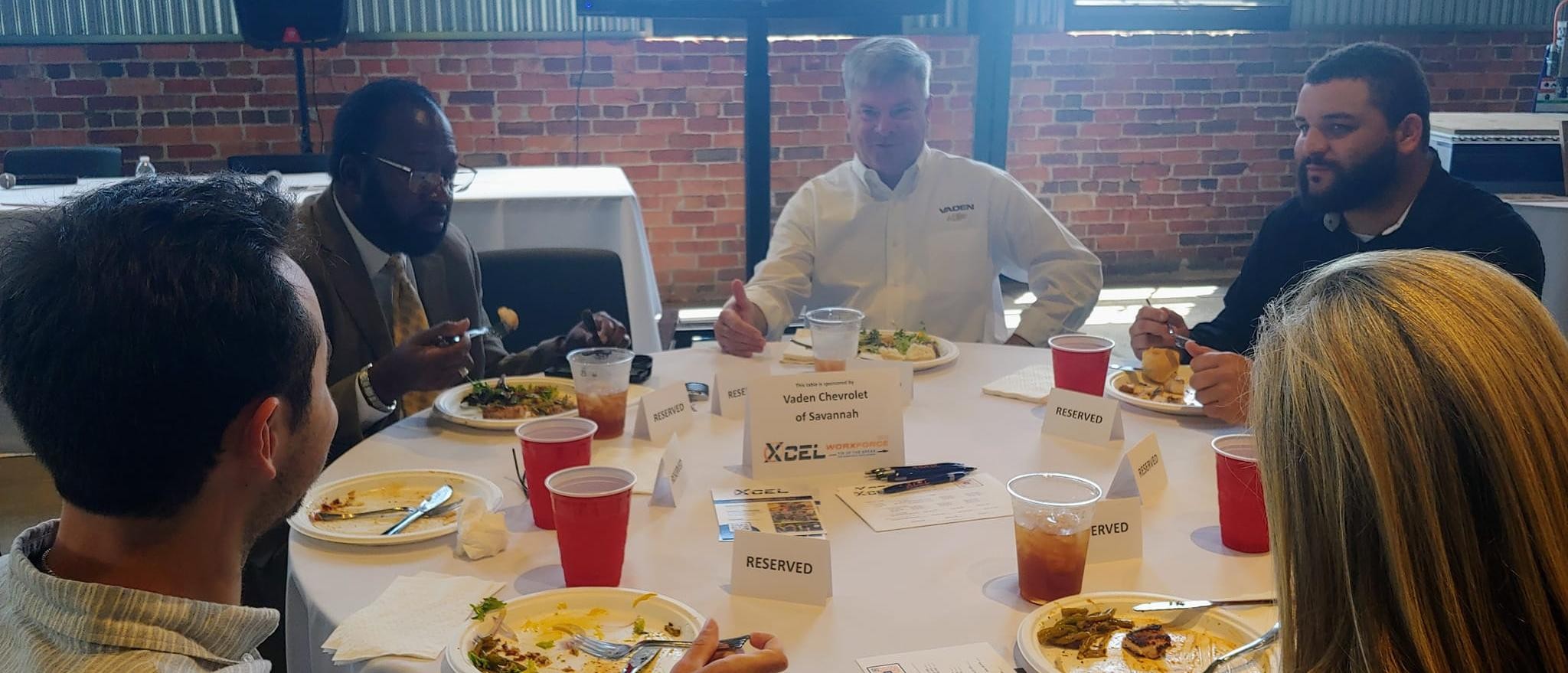 General Manager, Neal Wilson, sits at a round table to have lunch with other team members and Savannah Arts work-based learning advisor, Dr. Willis Blake. 