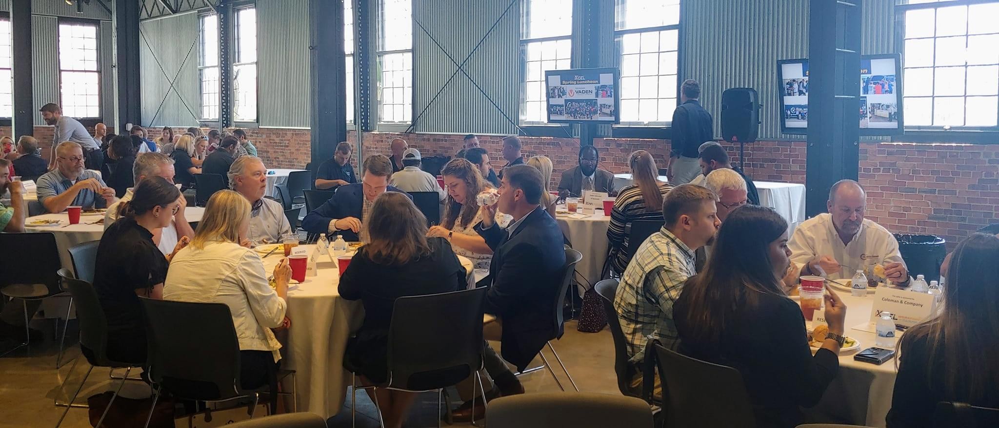 A photo of various tables filled with people eating together during Xcel Strategies Spring Lunch event