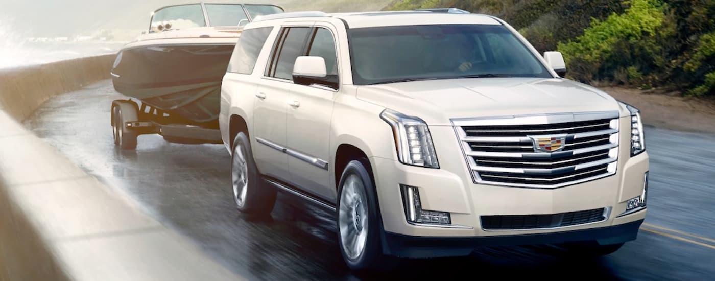 A white 2020 Cadillac Escalade is towing a boat around a corner near the water while on vacation after leaving a Cadillac dealer near me in Fort Worth, TX.