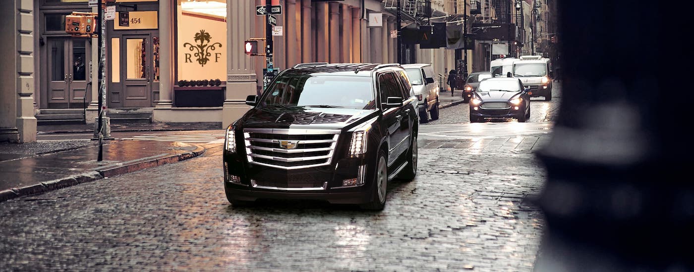 A black used Cadillac SUV, a 2017 Cadillac Escalade, is driving on a street near Fort Worth, TX, after the rain.