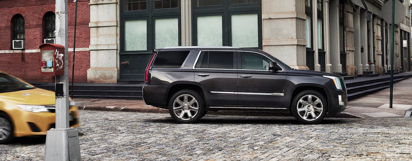 A popular pre-owned Cadillac, a dark gray 2017 Cadillac Escalade, is parked on a cobblestone street near Fort Worth, TX.