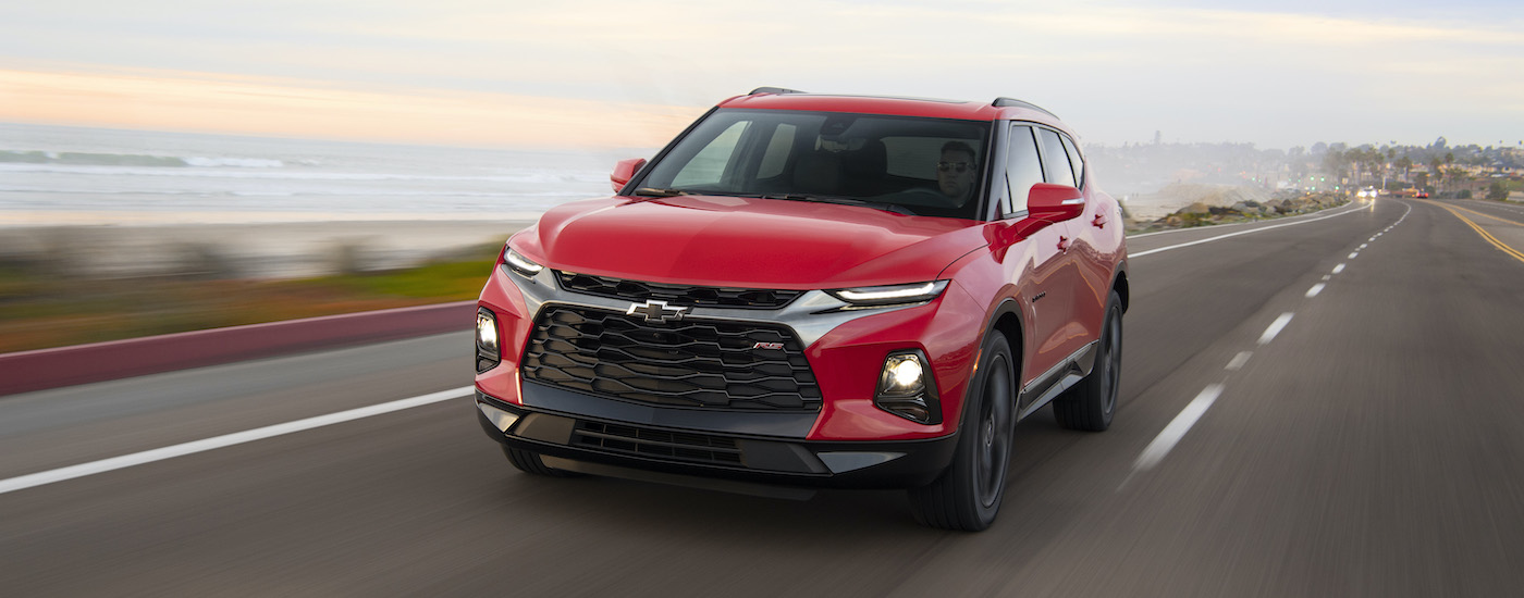 A popular Chevy SUV,  a red 2020 Chevy Blazer RS, is driving down the highway away from a city.