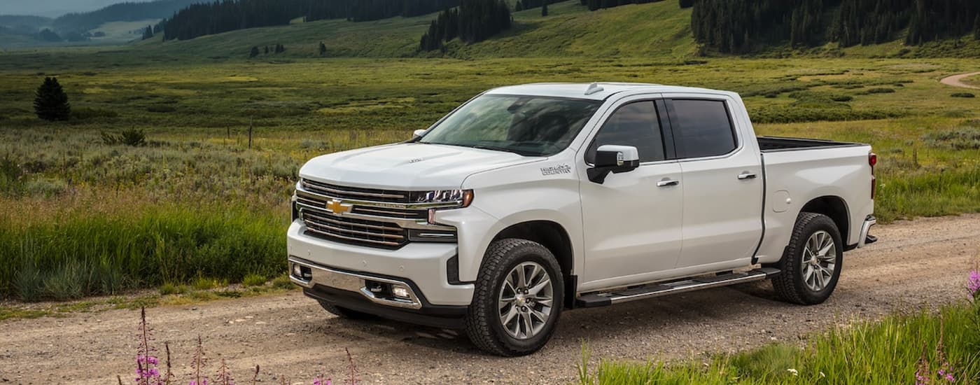 A white 2021 Chevy Silverado 1500 is driving on a rural dirt road after leaving a Booneville GM dealership.