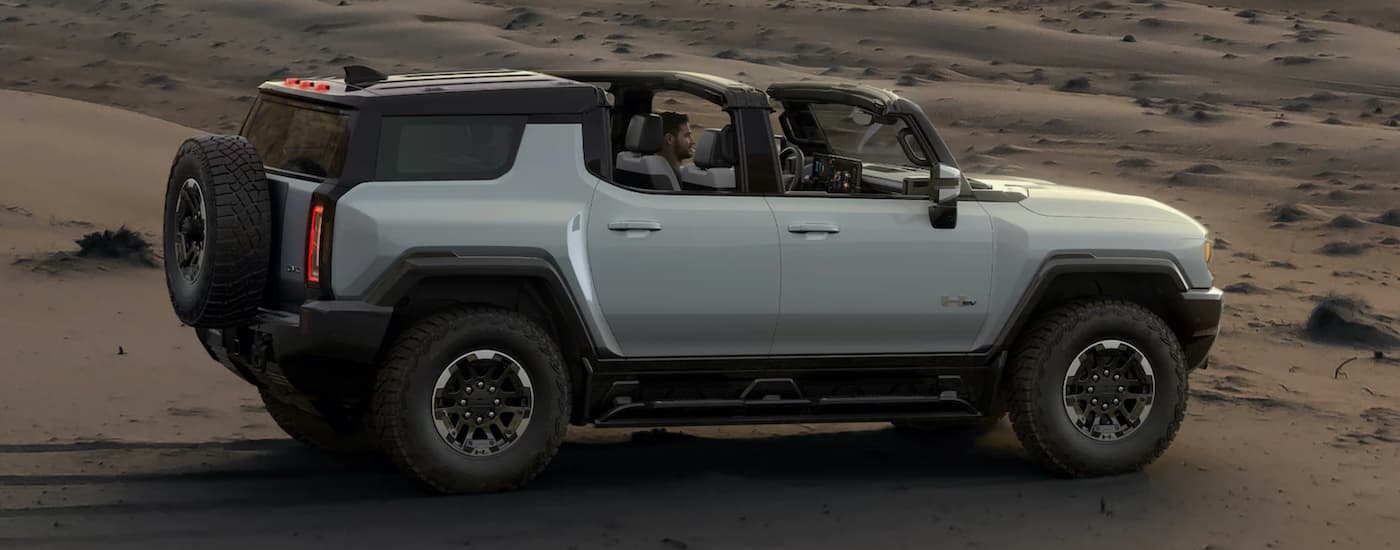A silver 2022 GMC Hummer EV SUV from an electric car dealership in MS is parked on sand with the roof off.