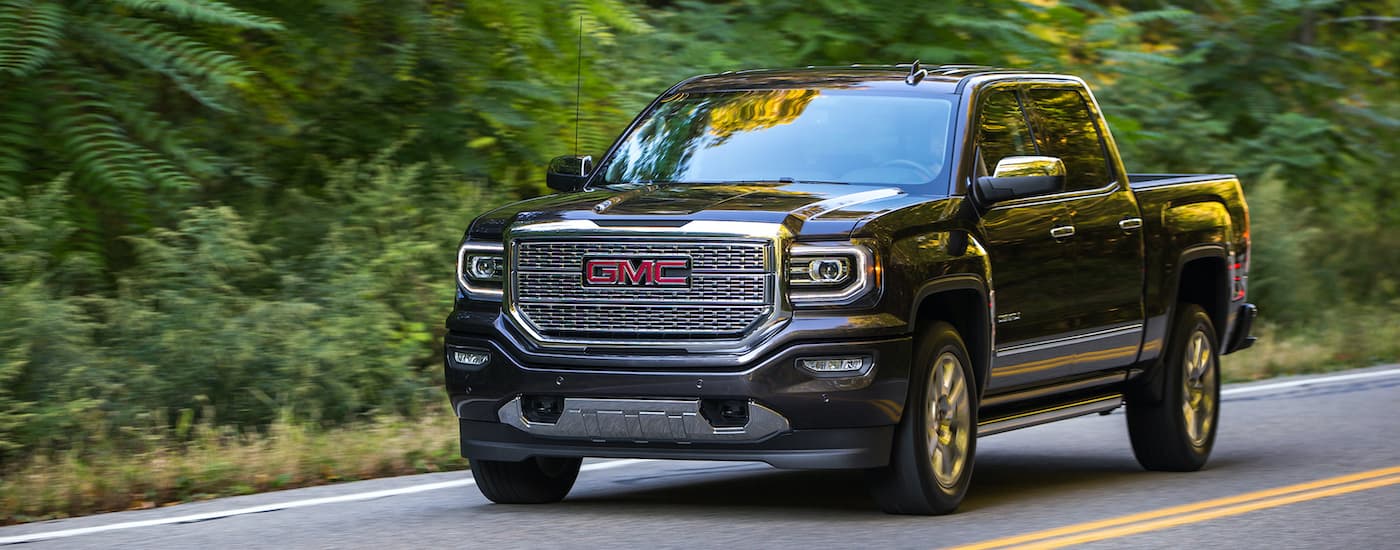 A black 2016 GMC Sierra 1500 Denali is shown driving down a road after leaving a used GM dealership.