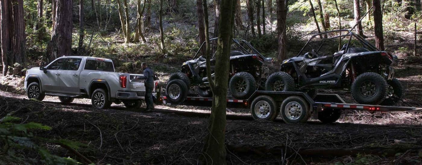 A white 2022 GMC Sierra 1500 AT4 is shown pulling an open trailer with two ATVs