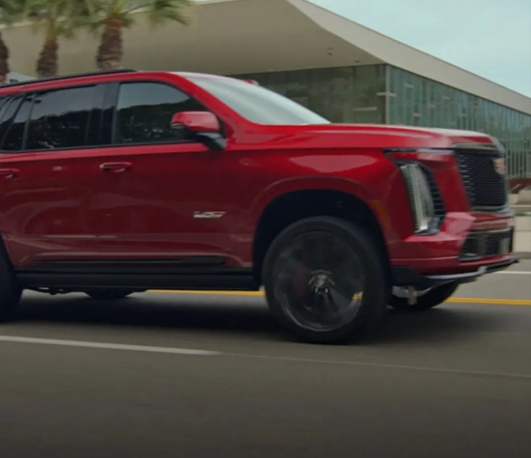 Cadillac Escalade SUV Driving in motion down a street in front of a building