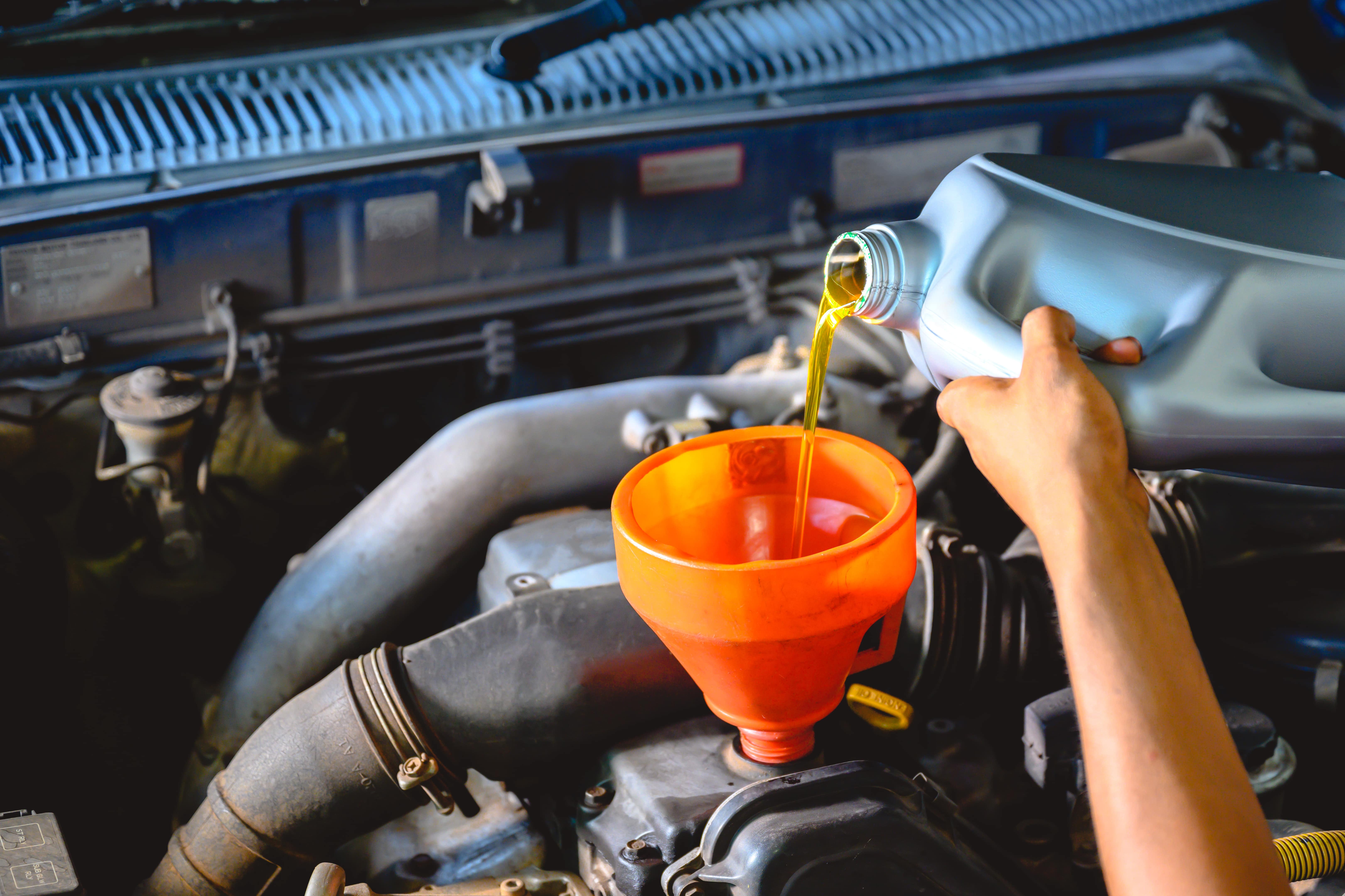 person adding oil to an engine with a funnel