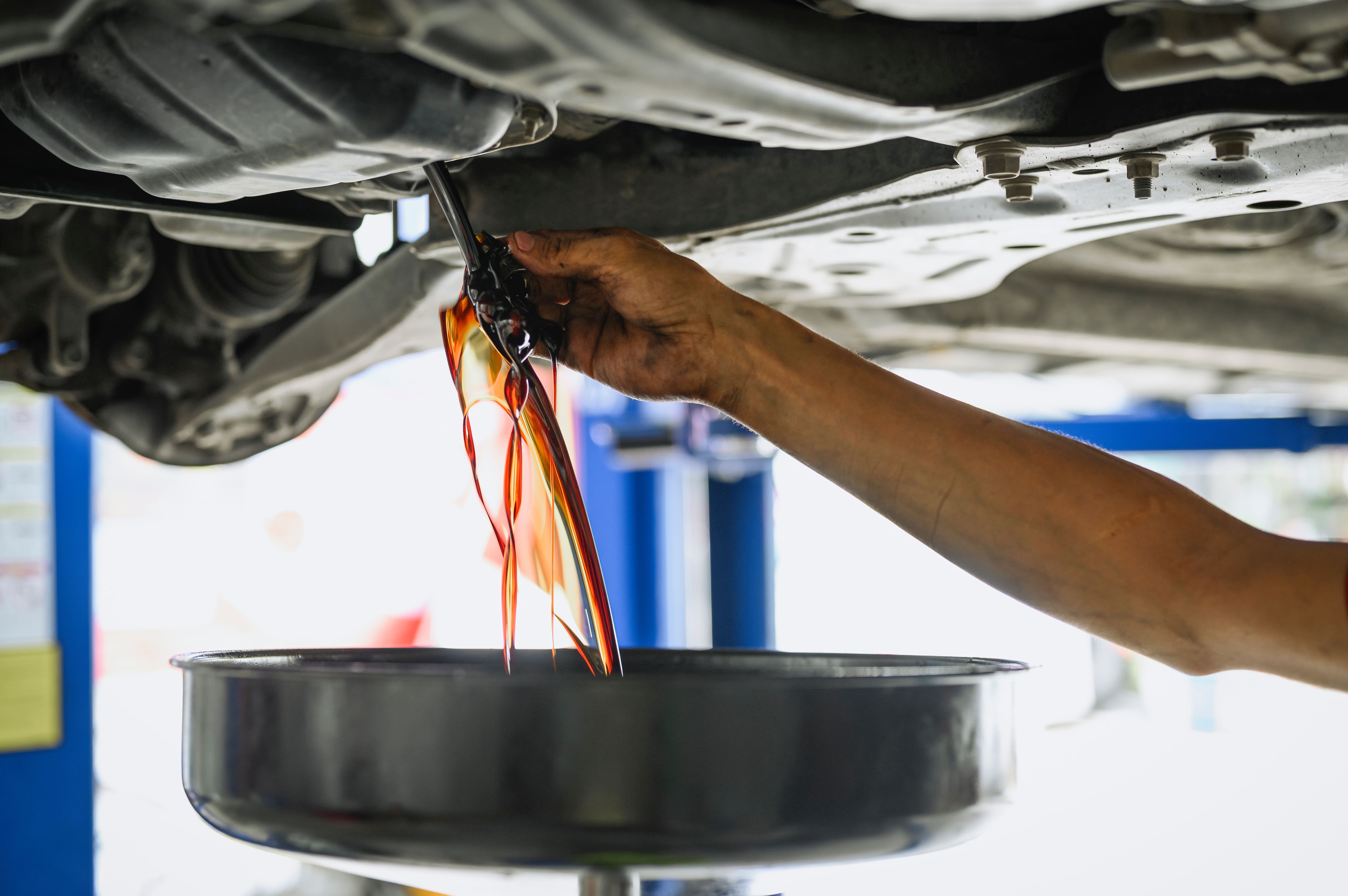 mechanic draining the oil from the underside of an SUV