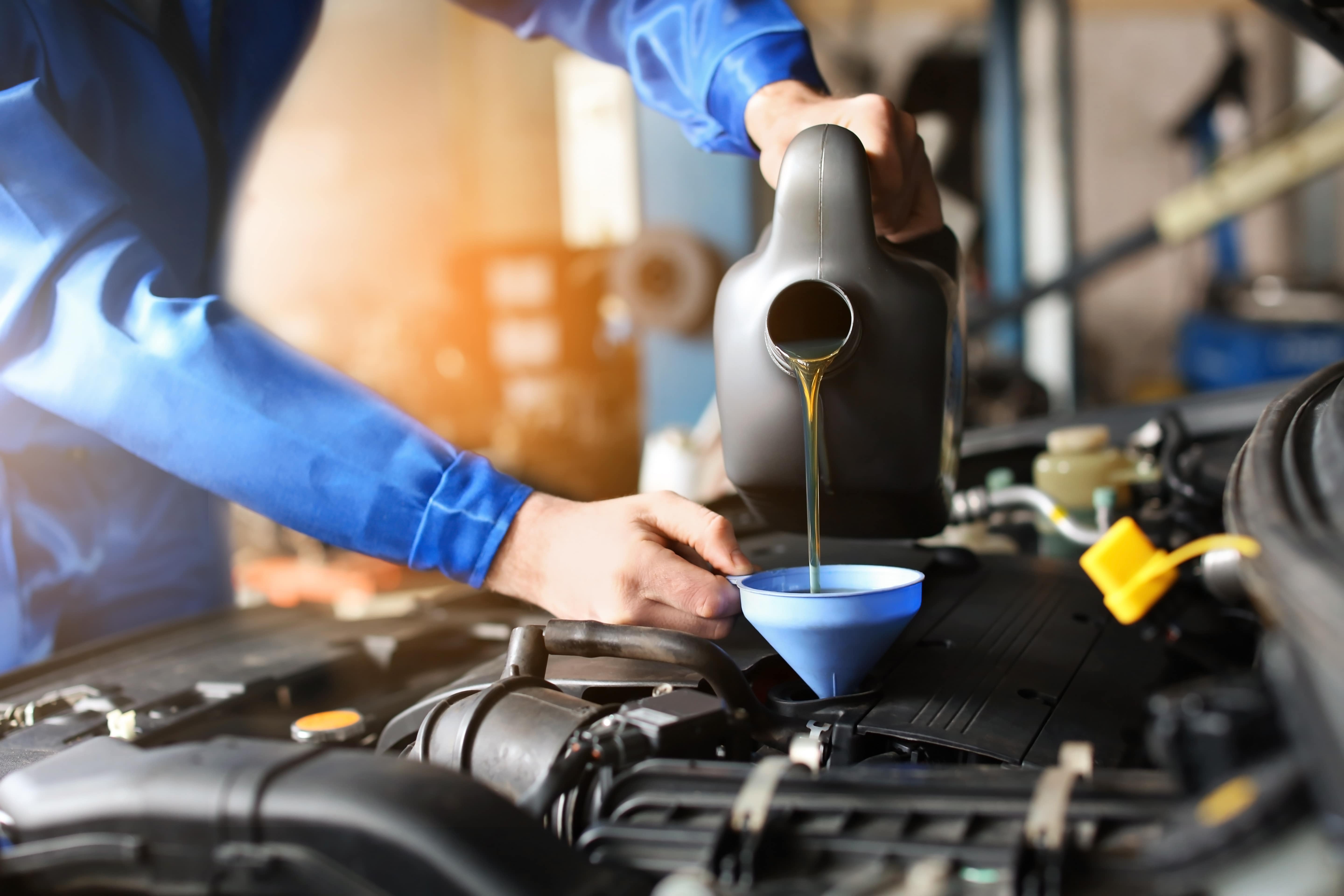 mechanic in uniform adding oil to an ICE engine via a funnel