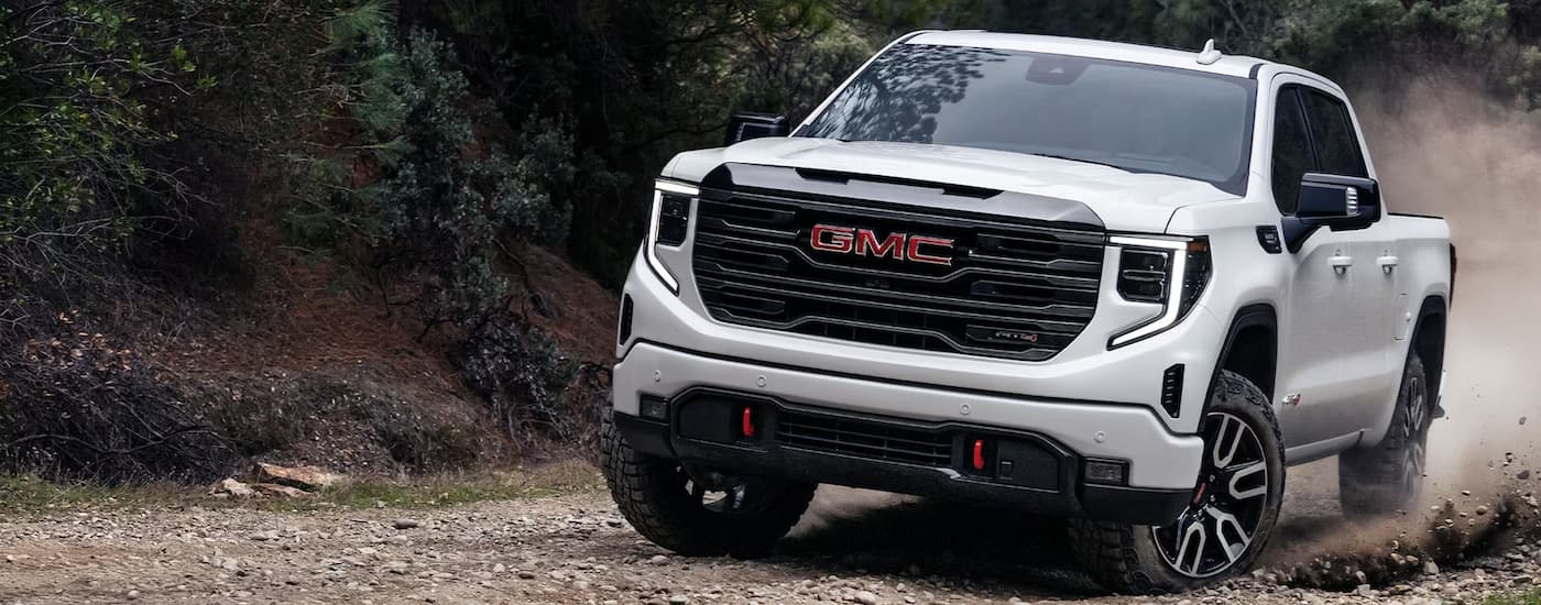 A white 2024 GMC Sierra 1500 AT4 is off-roading on a rocky trail after leaving a GMC dealer.