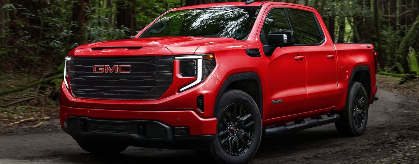 A red 2024 GMC Sierra 1500 Elevation is driving on a dirt road after leaving a GMC dealer.
