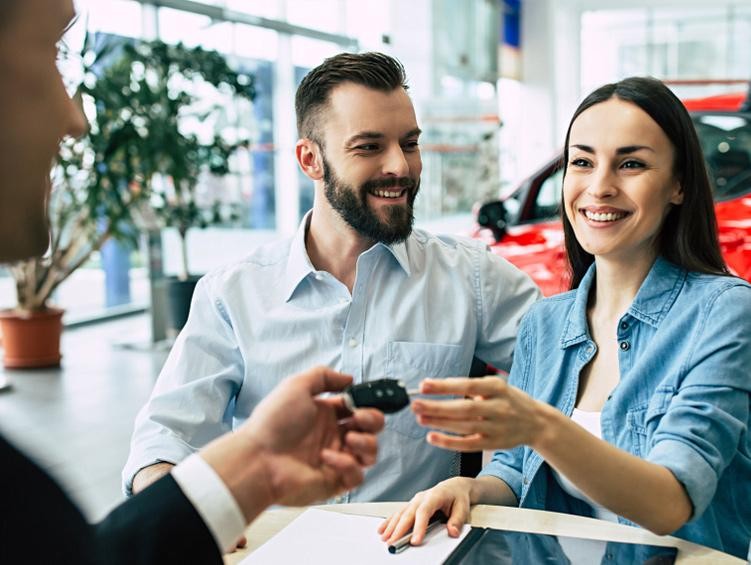 Salesman at a dealership handing over the car keys for a couple's new purchase