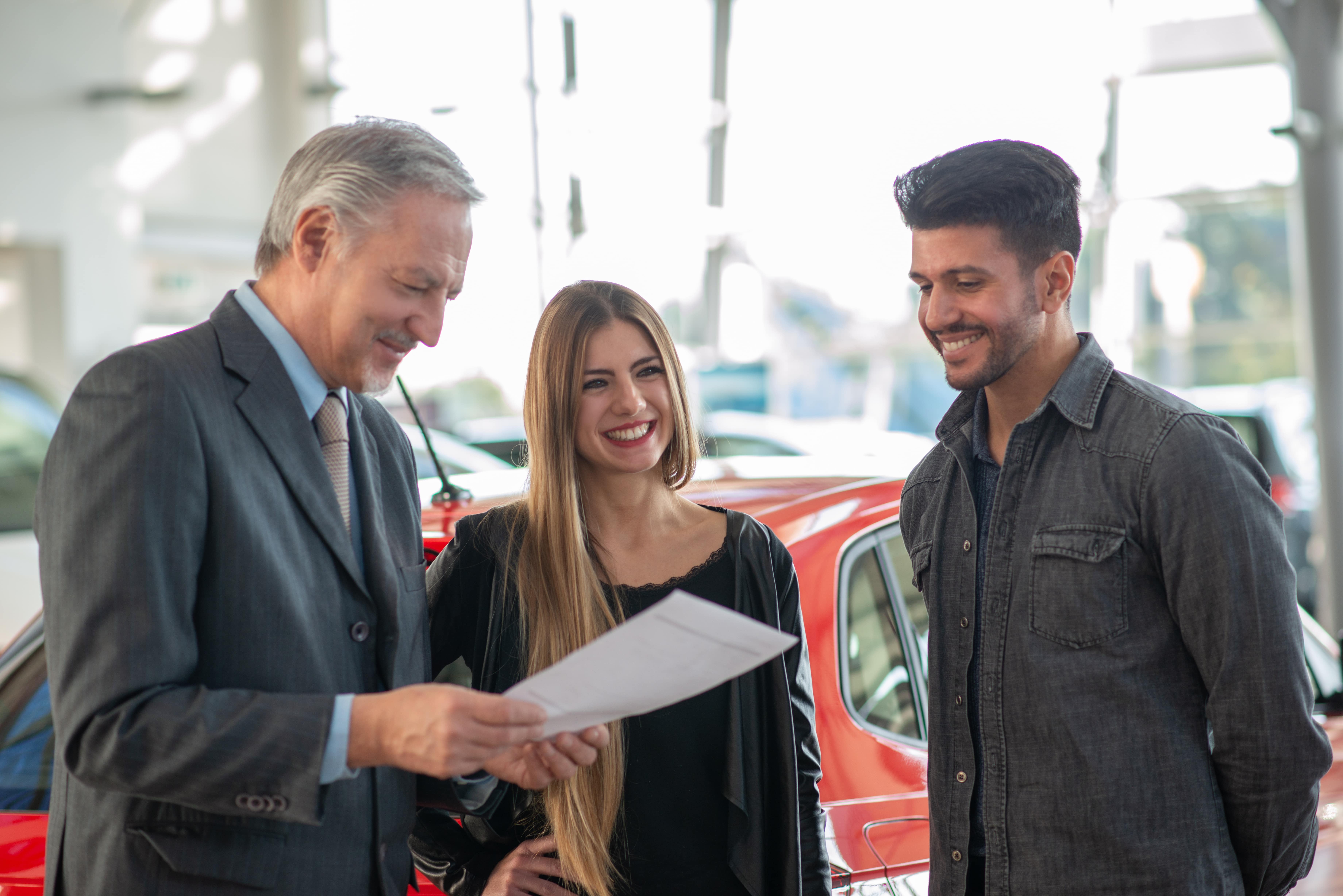 Car salesman talking to a happy couple while reviewing paperwork