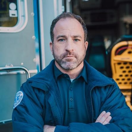 Male Paramedic Posing In Front Of Ambulance