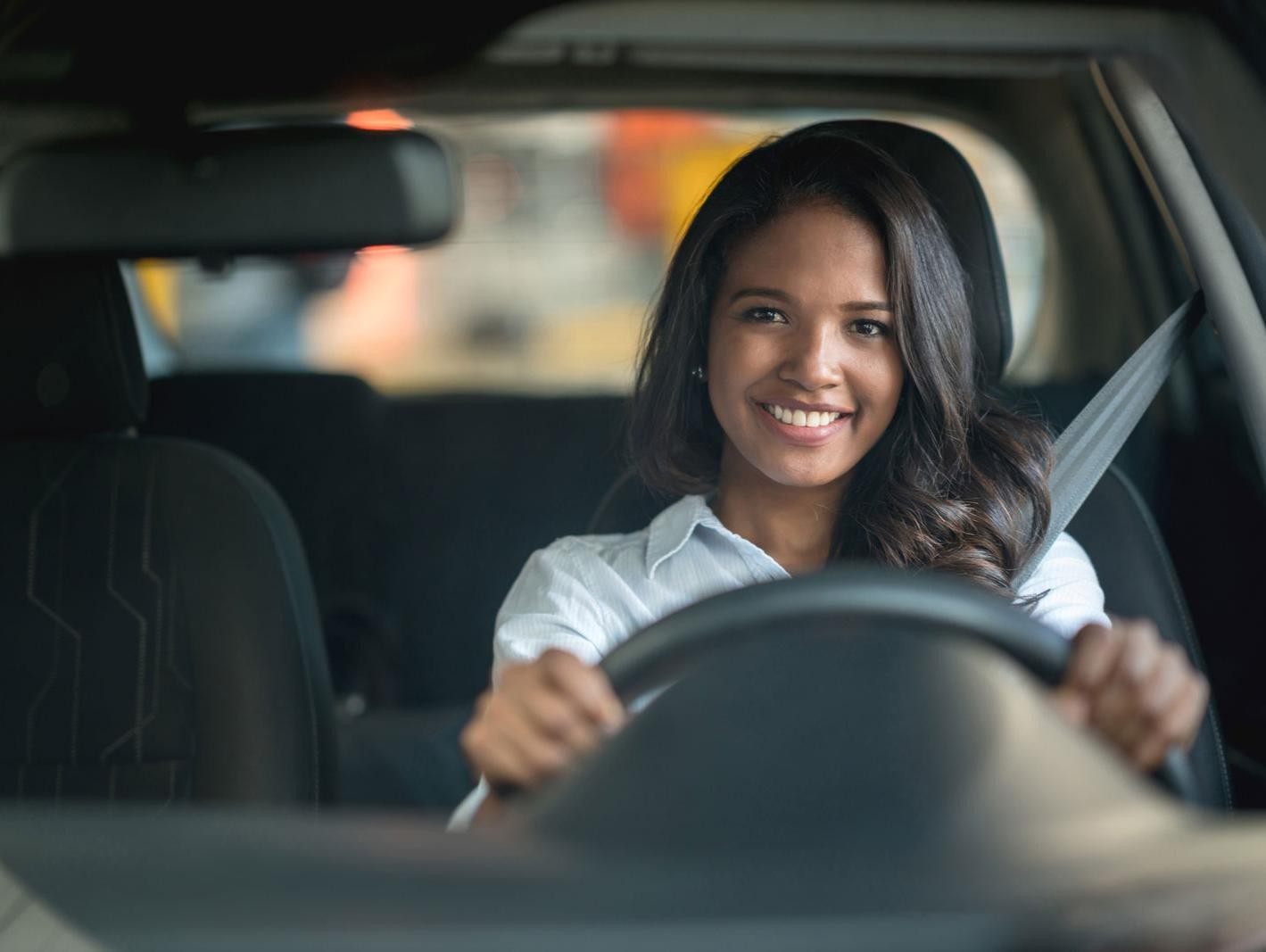 Happy woman driving a car at the dealership