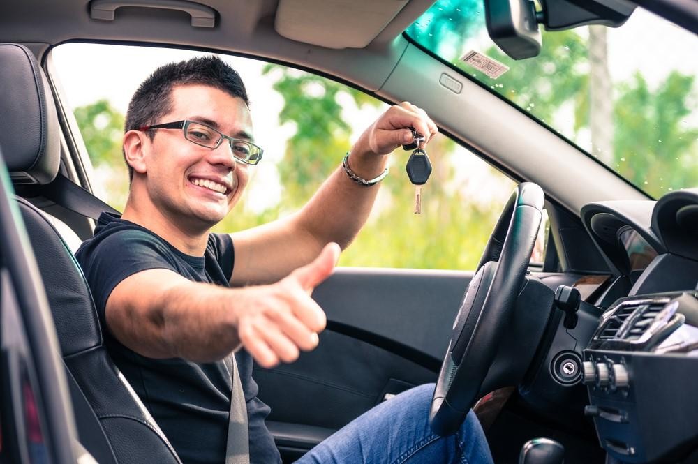 Young man in a car holding keys giving a thumbs up