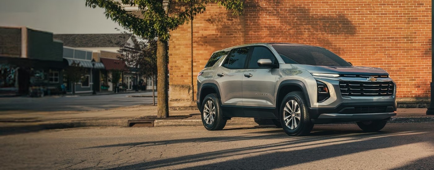 A silver 2025 Chevy Equinox for sale in Alexandria is parked next to a brick wall.