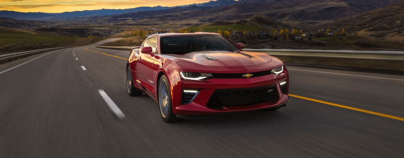 A red 2017 Chevy Camaro is driving on an open road after viewing used cars for sale.