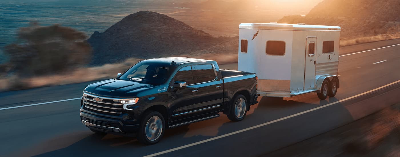 A black 2022 Chevy Silverado 1500 High Country is towing a white enclosed trailer.
