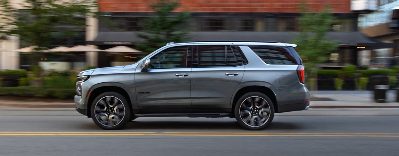A grey 2025 Chevy Tahoe for sale is driving on a city street.